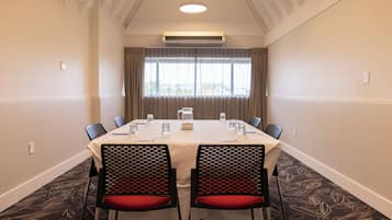 Un salón de conferencias con una mesa, sillas y un ventanal con cortinas.