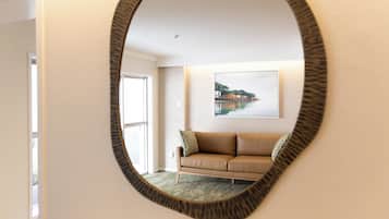 A room with a circular mirror reflecting a beige sofa and a framed picture of a coastal landscape.