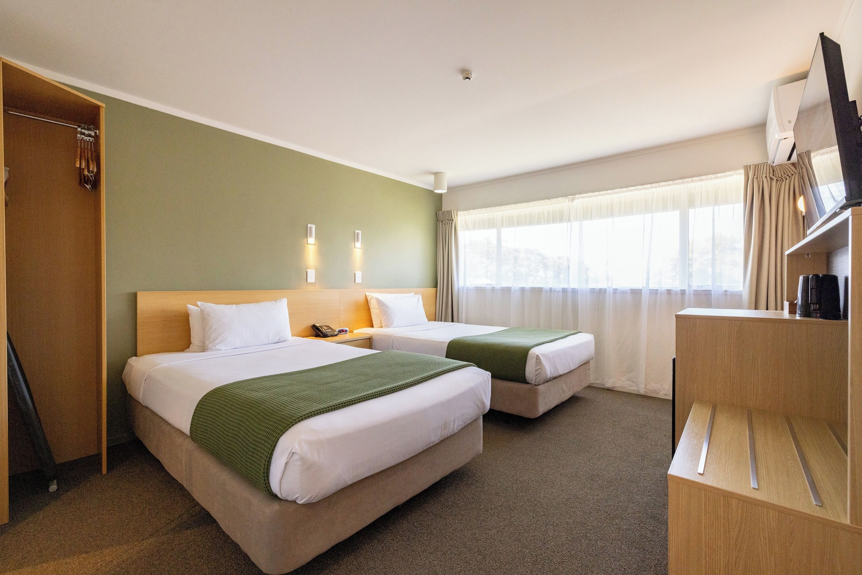 Une chambre d’hôtel avec deux lits, un bureau, une armoire et un téléviseur.