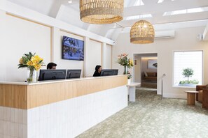 A reception area with a reception desk, two computer monitors, and a television displaying a restaurant. - Auckland Rose Park Hotel (Auckland)