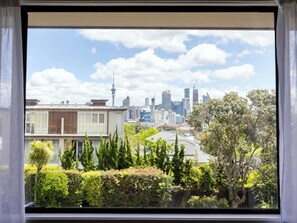 A cityscape with modern buildings and a prominent tower, viewed through a window with a view of a well-maintained garden. - Auckland Rose Park Hotel (Auckland)