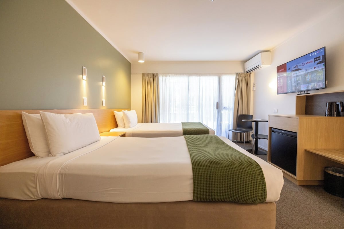 A hotel room with two beds, a desk, a television, and a window with curtains.