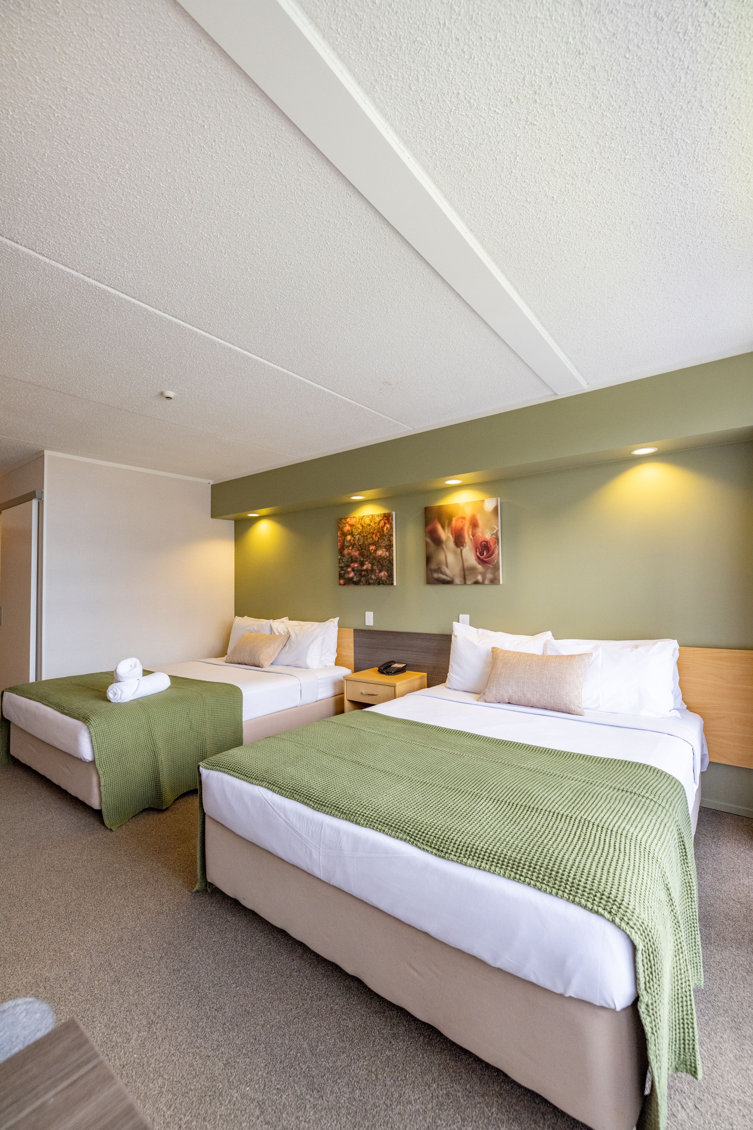 A hotel room with two beds, a green wall, and artwork.