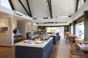 Una cafetería moderna con una isla de servicio central, zona de estar y grandes ventanales.