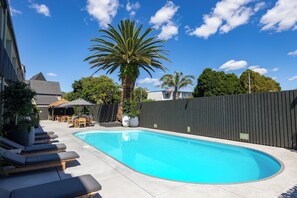 A swimming pool with lounge chairs, a wooden fence, and a palm tree. - Auckland Rose Park Hotel (Auckland)
