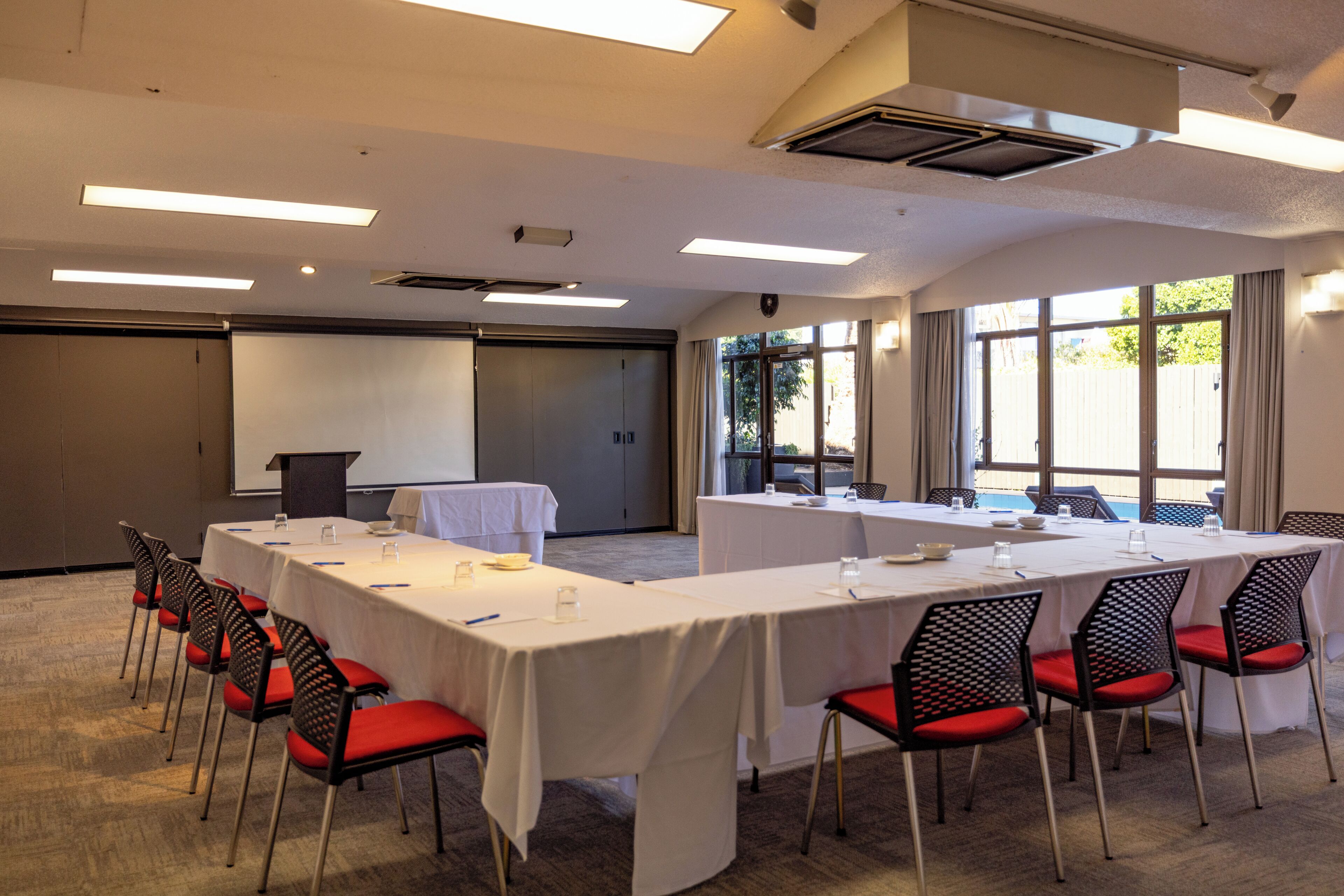 Un salón de conferencias con mesas, sillas, una pantalla de proyector y un ventanal grande.