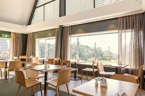 A hotel room with a dining area, large windows, and a view of the outdoors.