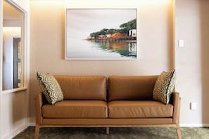 A tan leather sofa with patterned cushions against a wall, with a framed landscape painting above it.