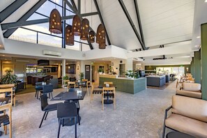 Um espaço amplo e interno, com pé direito alto, diversos arranjos de assentos e um bar central.