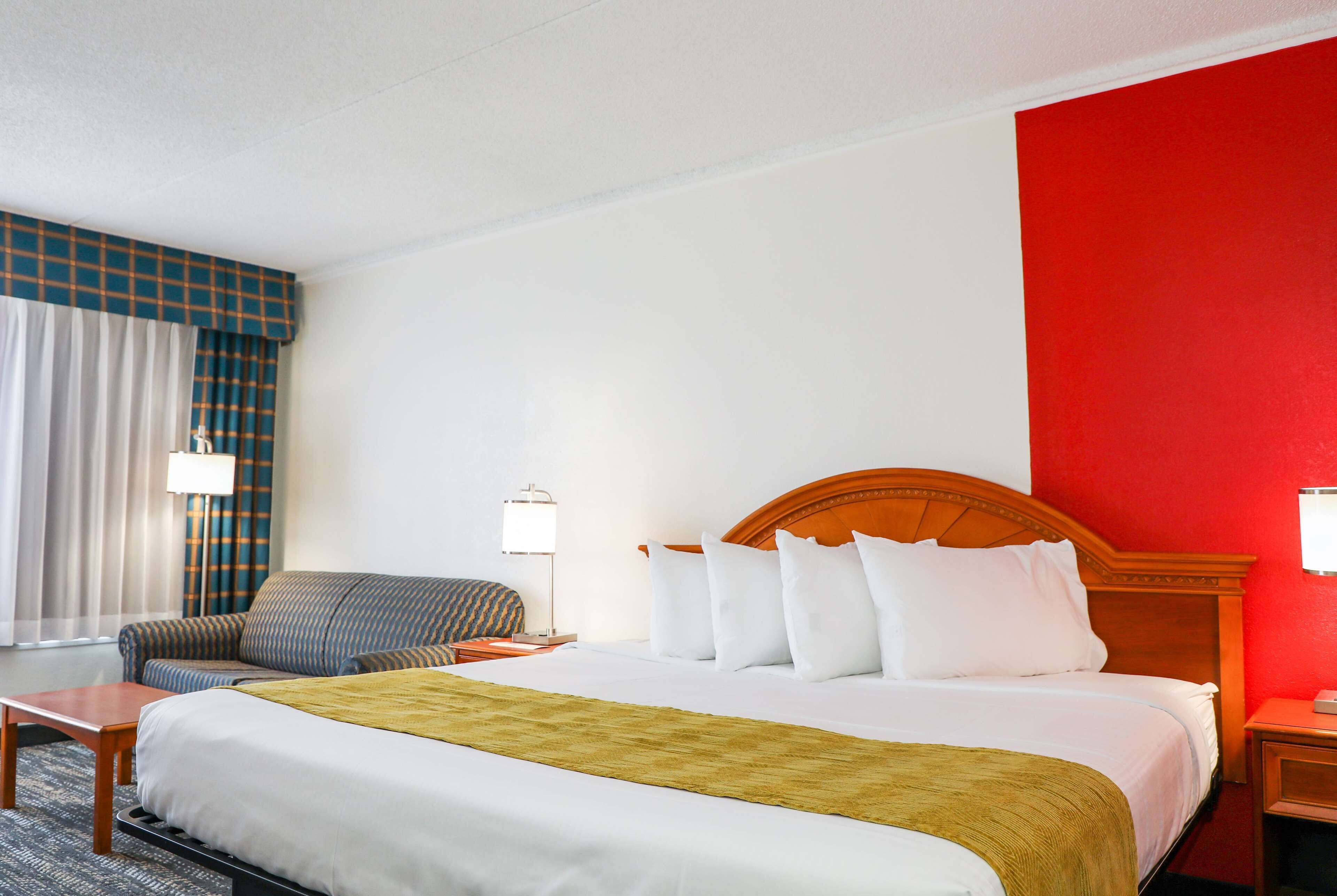 A hotel room with a bed, a sofa, a nightstand, and a lamp.
