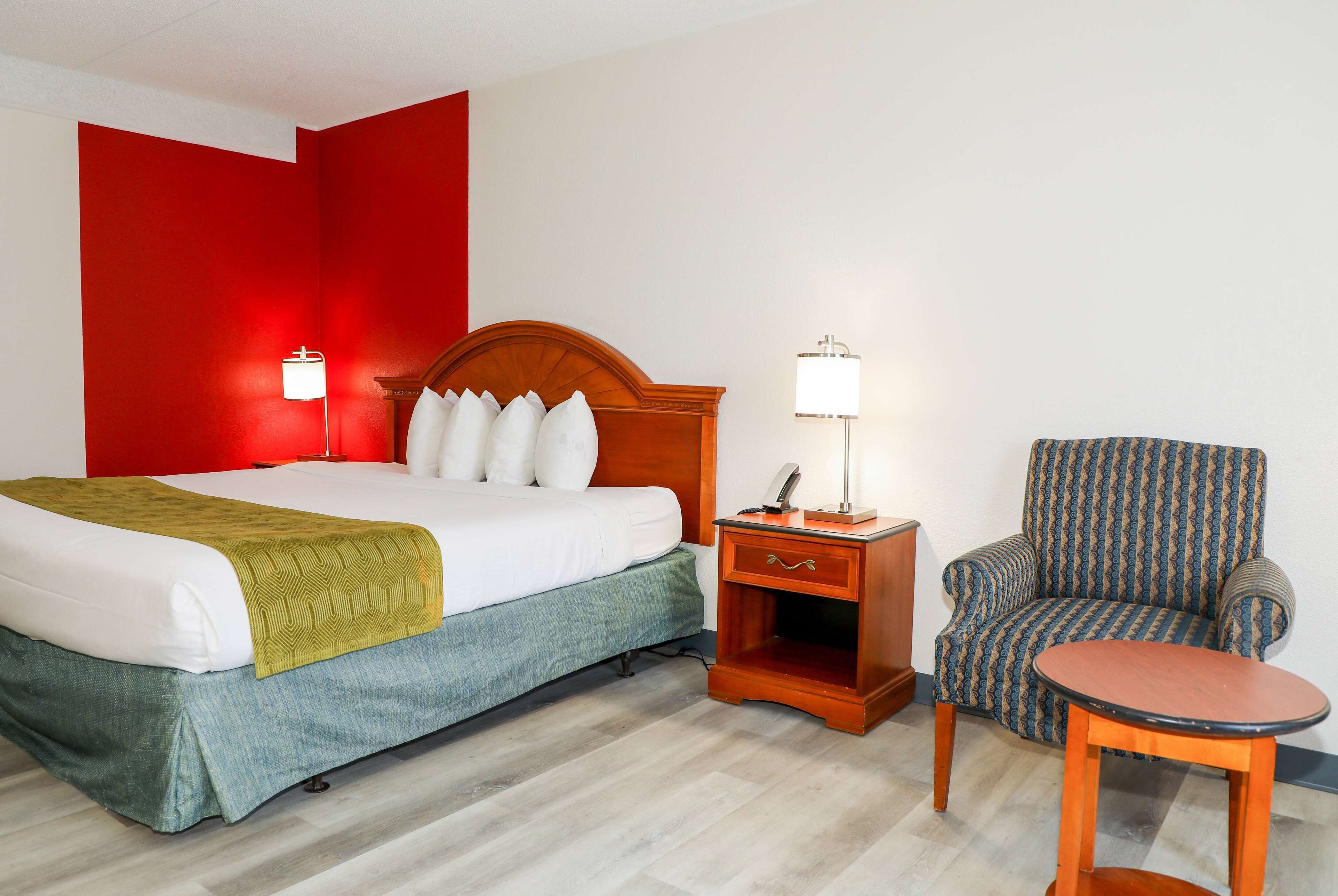 A hotel room with a bed, a nightstand, a chair, and a small table.
