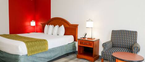 A hotel room with a bed, a nightstand, a chair, and a small table.