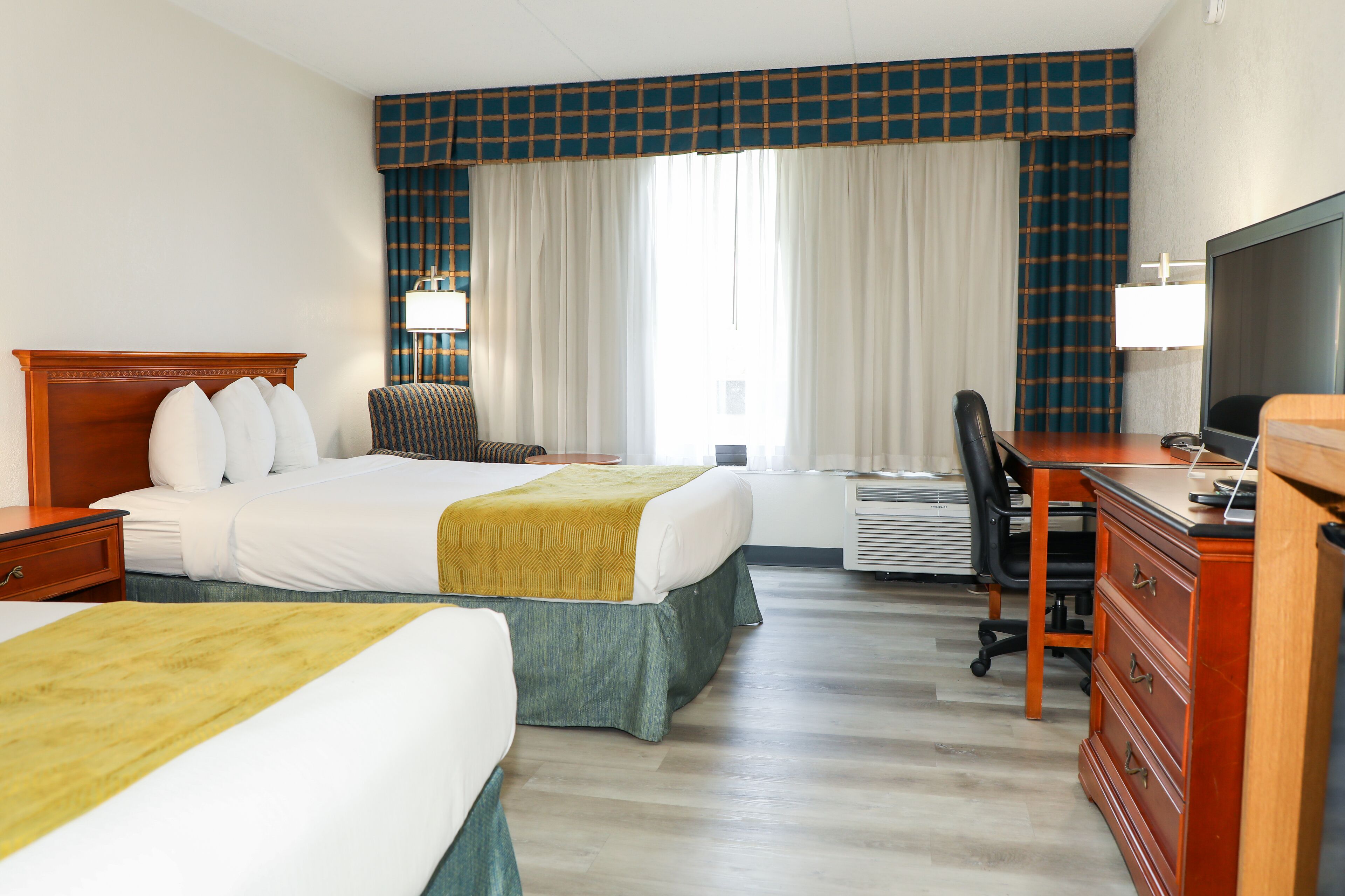 Ein Hotelzimmer mit zwei Betten, einem Schreibtisch, einem Stuhl, einem Fernseher und einer Klimaanlage.