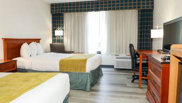 Ein Hotelzimmer mit zwei Betten, einem Schreibtisch, einem Stuhl, einem Fernseher und einer Klimaanlage.