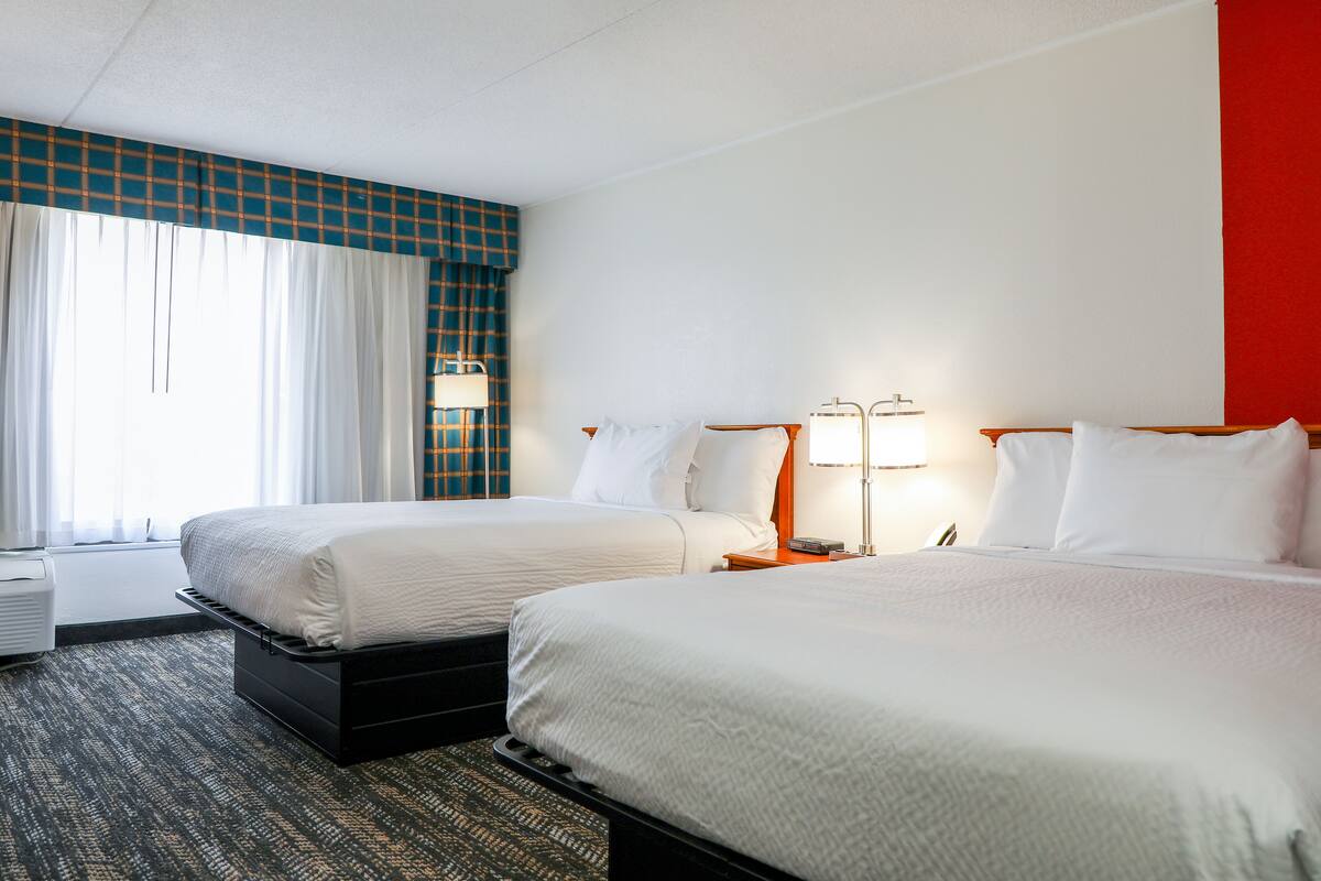 Habitación de hotel con dos camas, un ventanal con cortinas, un televisor de pantalla plana y un escritorio con lámpara.