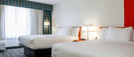 A hotel room with two beds, a large window with curtains, a flat-screen TV, and a desk with a lamp.