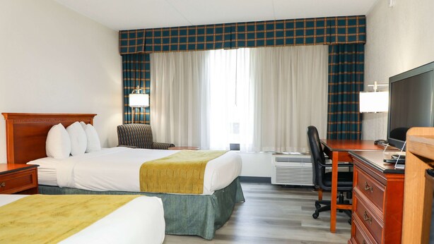 Ein Hotelzimmer mit zwei Betten, einem Schreibtisch, einem Sessel, einem Fernseher und einem Fenster mit Vorhängen.