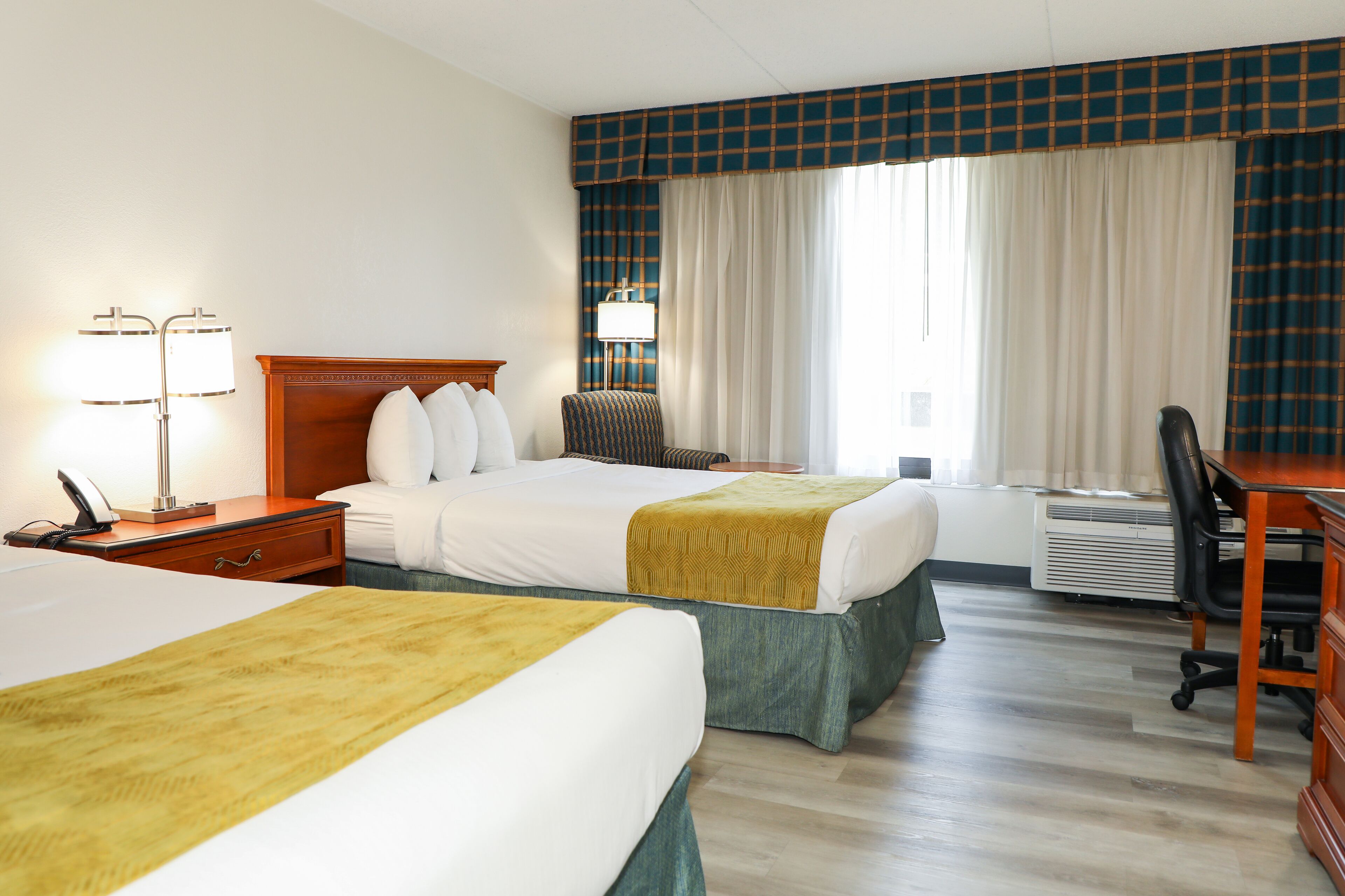 Une chambre d’hôtel avec deux lits, un bureau, une chaise, une lampe et un appareil de climatisation.