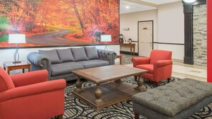 Eine Lobby mit einem großen Wandgemälde zum Thema Herbst, einem grauen Sofa, einem roten Sessel, einem Holztisch und einem gemusterten Teppich.