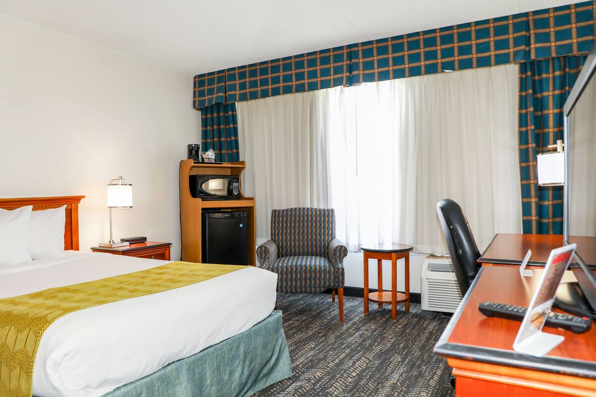 Habitación de hotel con una cama grande, un escritorio con computadora, una silla, una mesita, televisor y un minibar.