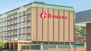 Ein Ramada Hotelgebäude mit gut sichtbarem Logo, einer Ziegel-Fassade und einem grünen Dach.