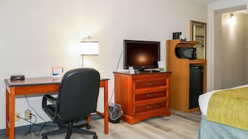 Hotellihuone, jossa on puinen työpöytä, musta toimistotuoli, televisio, mikroaaltouuni, pieni jääkaappi, keltainen peitto sängyllä ja peili sängyn yläpuolella.