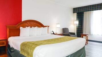 A hotel room with a large bed, a chair, a desk, and a lamp.