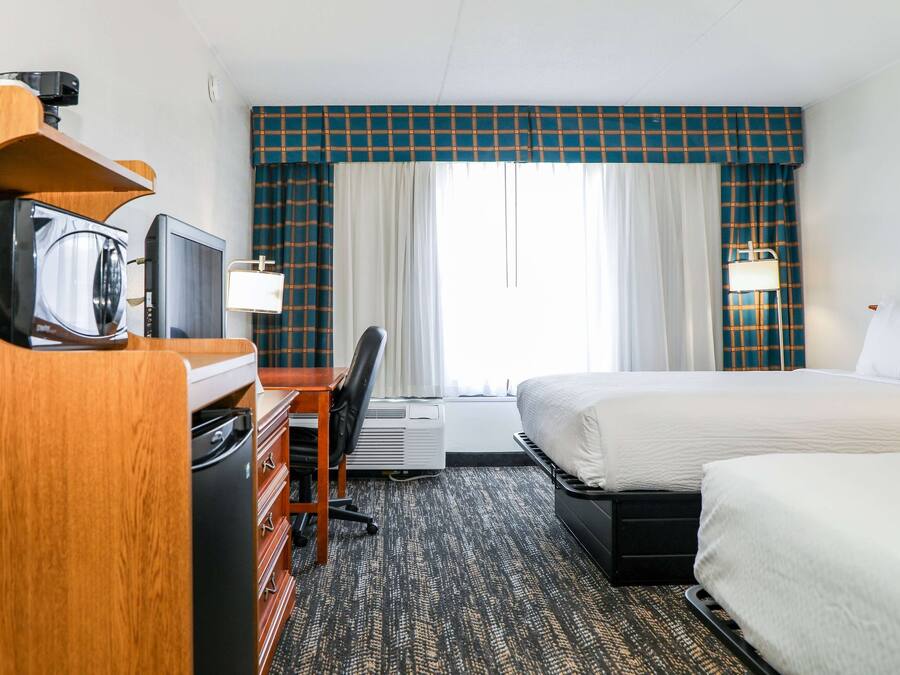 Quarto de hotel com uma cama, uma secretária com televisão, uma cadeira e uma janela com cortinas.