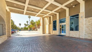 A covered outdoor area with a brick floor, stone walls, and a view of parked cars and palm trees.