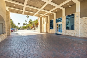 A covered outdoor area with a brick floor, stone walls, and a view of parked cars and palm trees. - Holiday Inn Express Anaheim West by IHG (Anaheim)