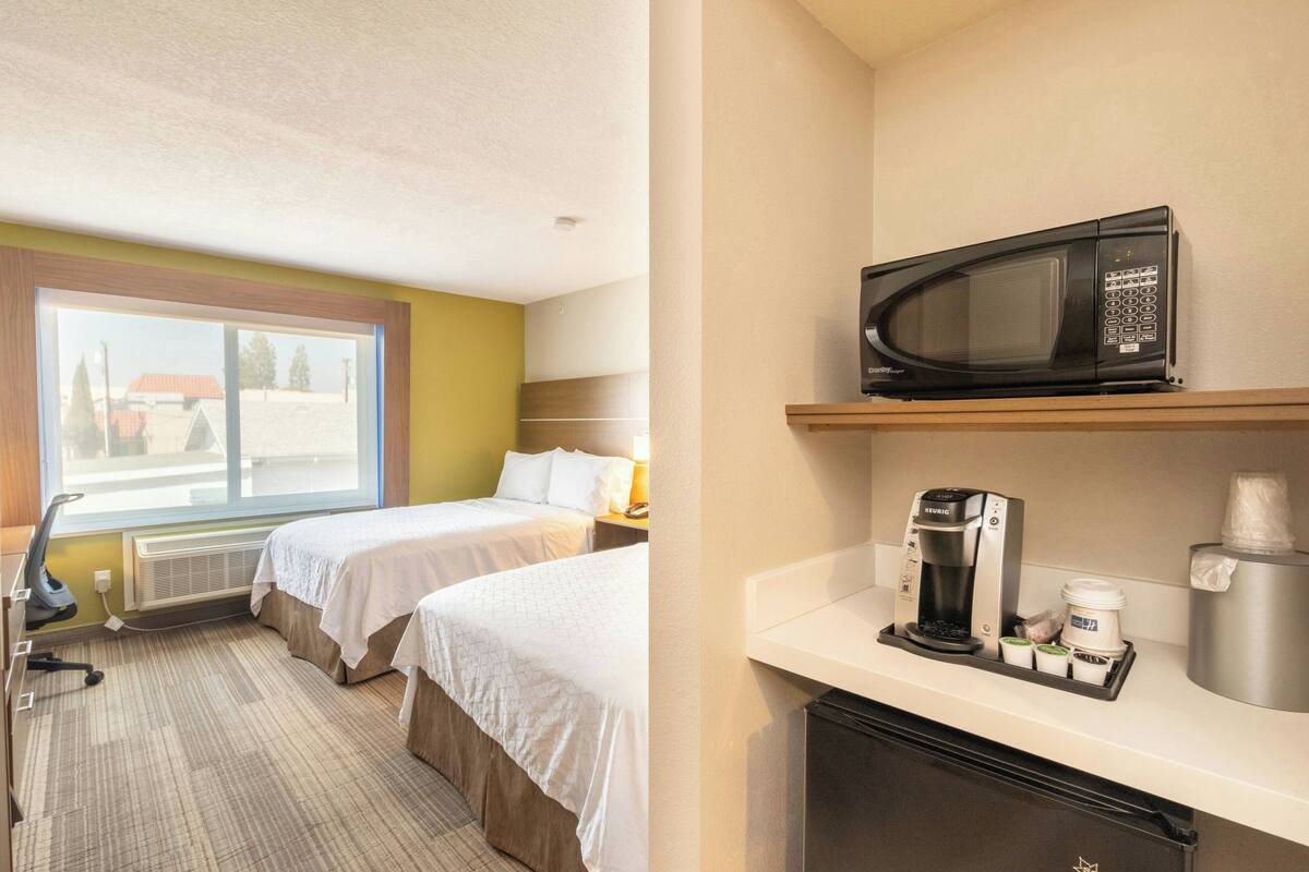 A hotel room with two beds, a microwave, a coffee maker, and a small refrigerator.