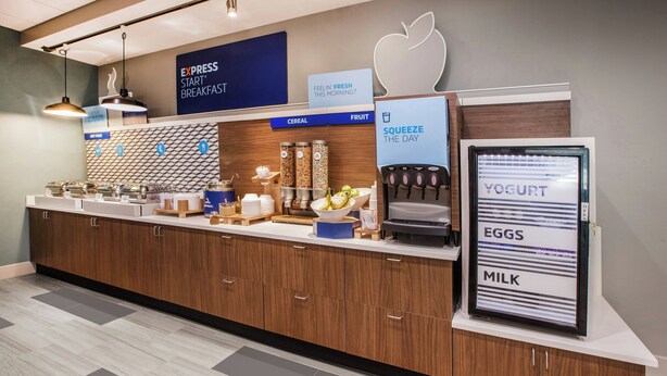 A modern breakfast bar with a coffee machine, cereal and fruit options, and a sign for yogurt, eggs, and milk. - Holiday Inn Express Anaheim West by IHG (Anaheim)