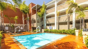 A swimming pool with a sun deck, palm trees, and a multi-story building with balconies. - Holiday Inn Express Anaheim West by IHG (Anaheim)