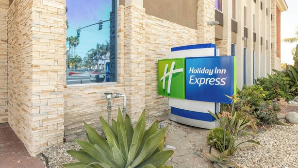 A Holiday Inn Express building with a stone facade, a large window, and a signboard. - Holiday Inn Express Anaheim West by IHG (Anaheim)