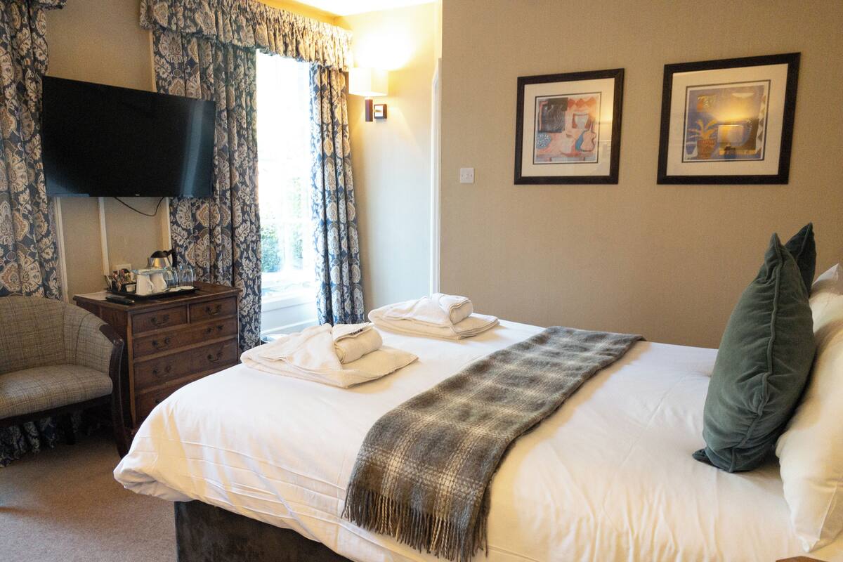 A hotel room with a large bed, a television on the wall, a dresser, and two framed pictures on the wall.