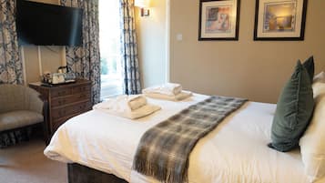 A hotel room with a large bed, a television on the wall, a dresser, and two framed pictures on the wall.
