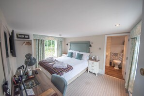 A hotel room with a bed, bedside table, desk, chair, and a bathroom with a toilet and sink.
