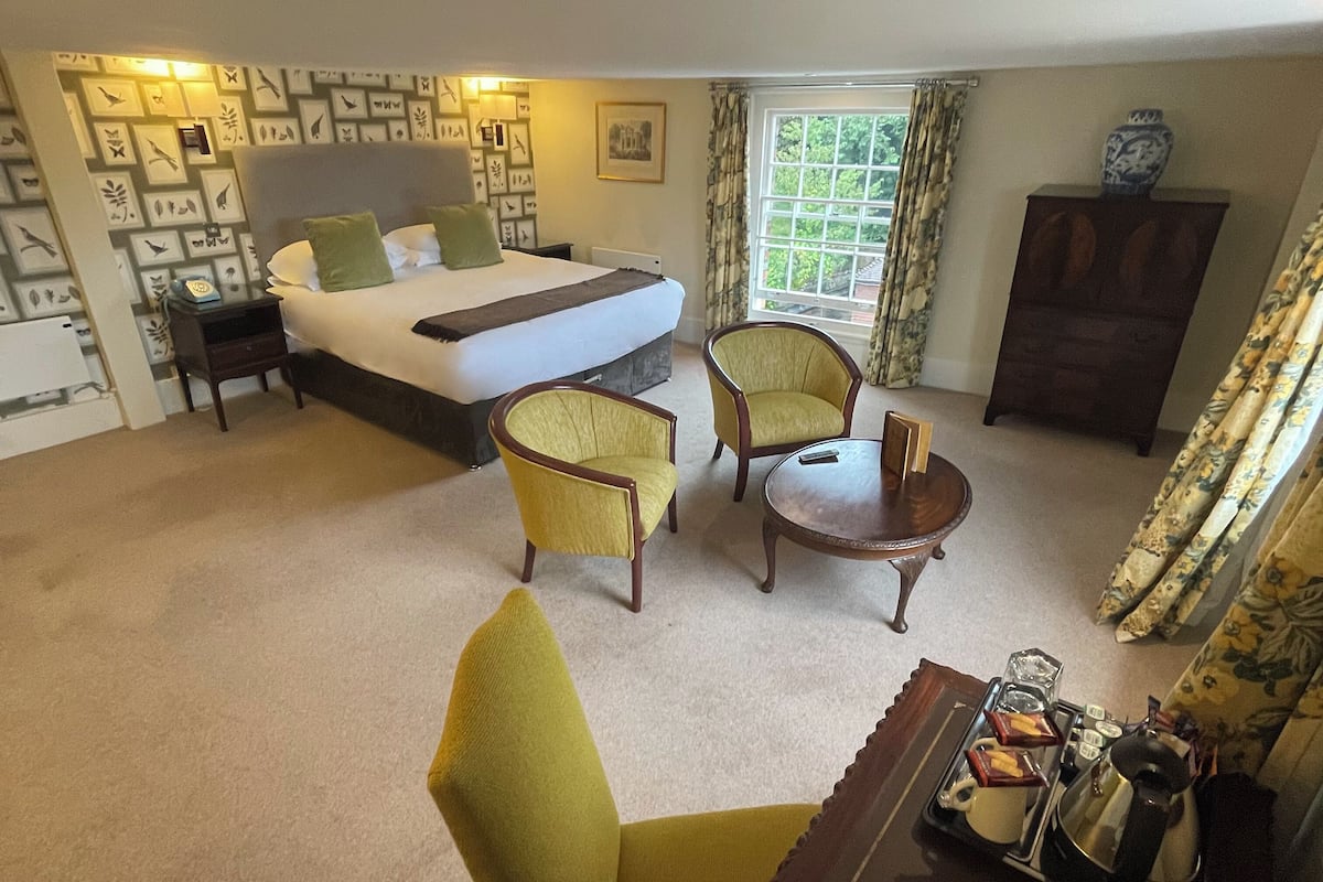 A hotel room with a bed, two armchairs, a small table, a cabinet, and a window with curtains.