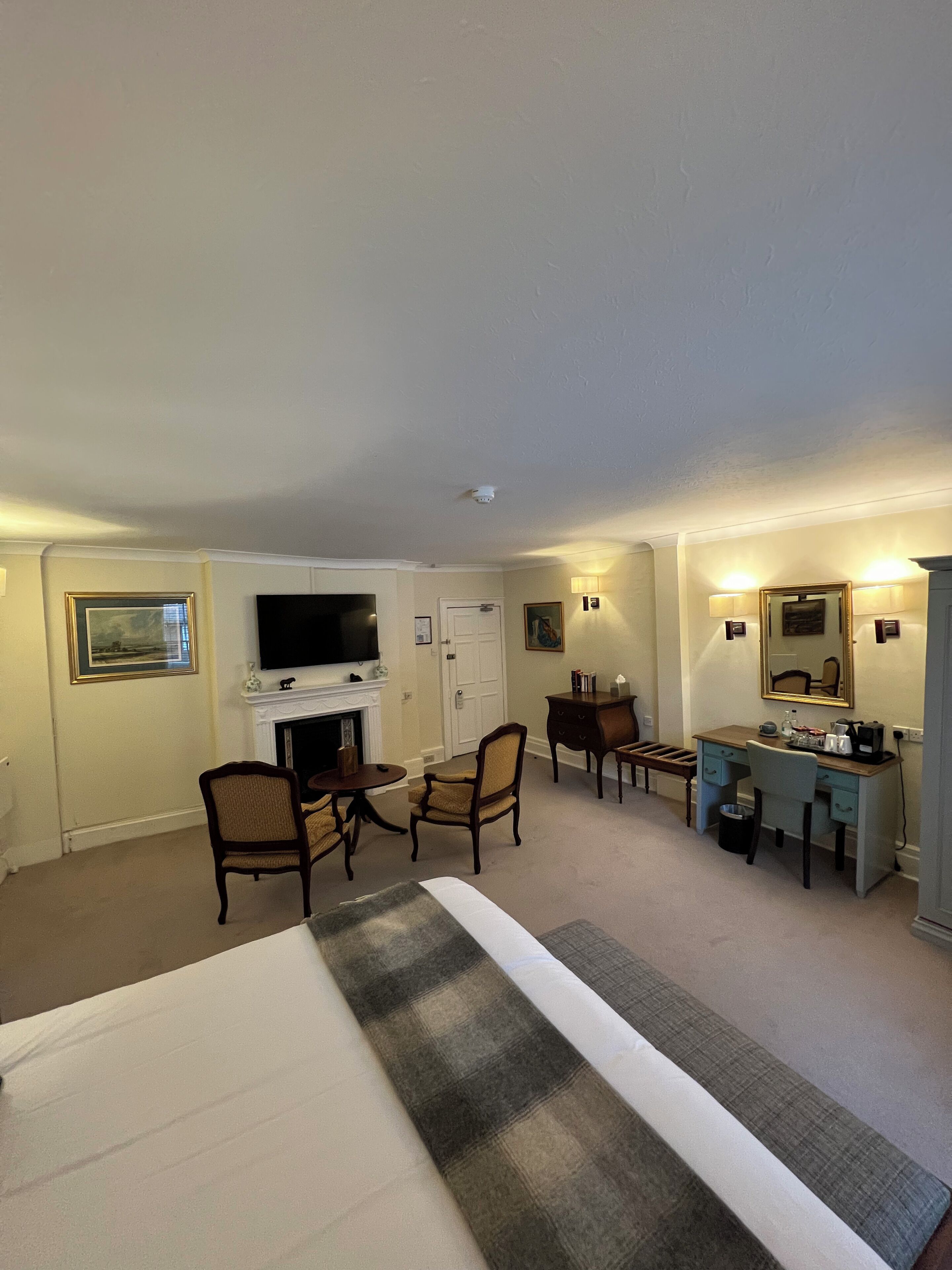 A hotel room with a bed, a desk, a chair, a television, a fireplace, and a mirror.
