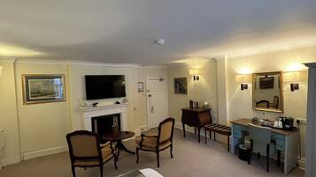 A hotel room with a bed, a desk, a chair, a television, a fireplace, and a mirror.