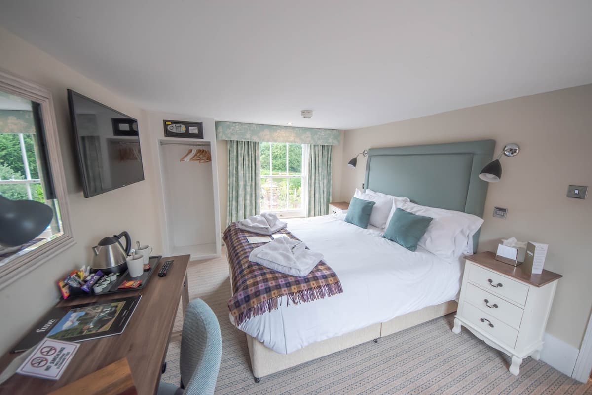A hotel room with a bed, bedside table, desk, and a window with curtains.