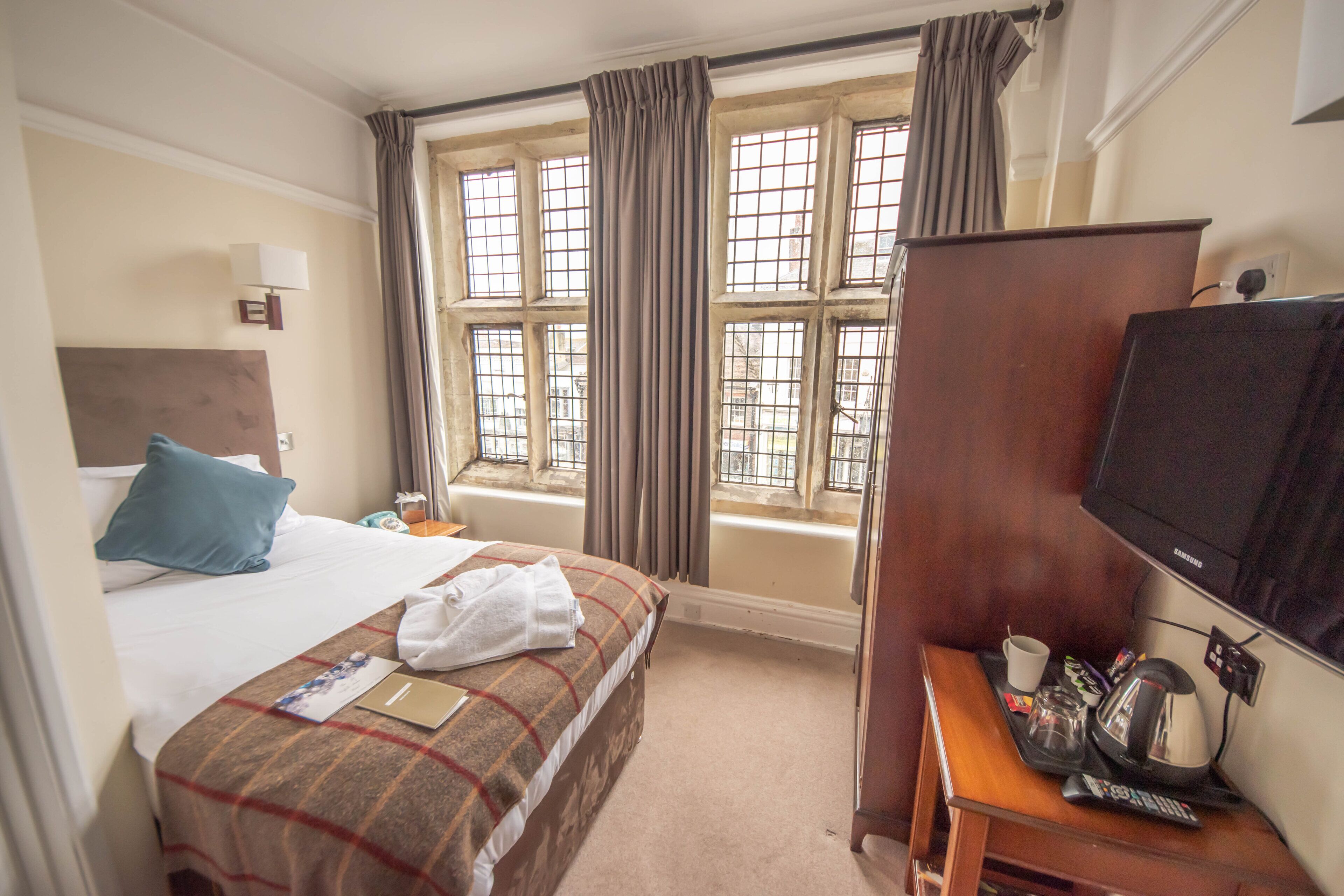 Habitación de hotel con cama, escritorio con televisor, ventana con cortinas y vista al exterior.