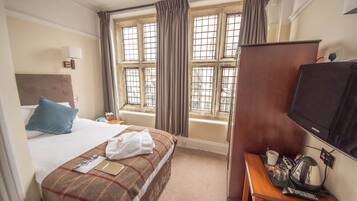 A hotel room with a bed, a desk with a television, a window with curtains, and a view of the outside.