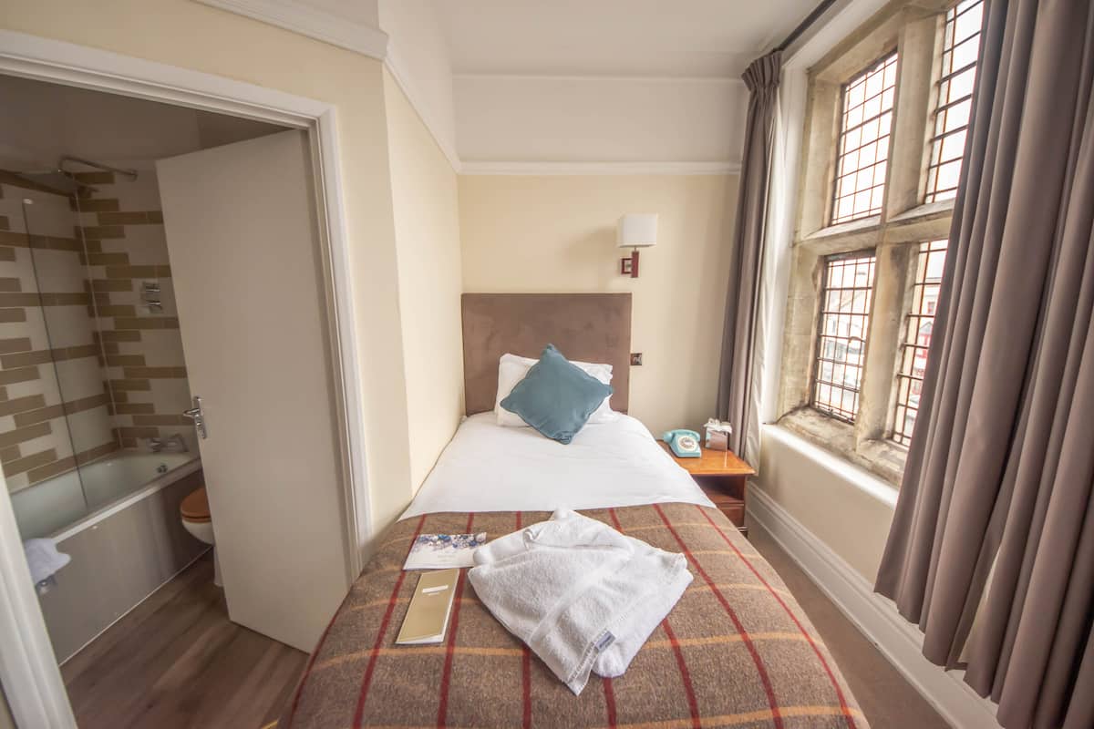 A hotel room with a bed, a bathroom, and a window with curtains.