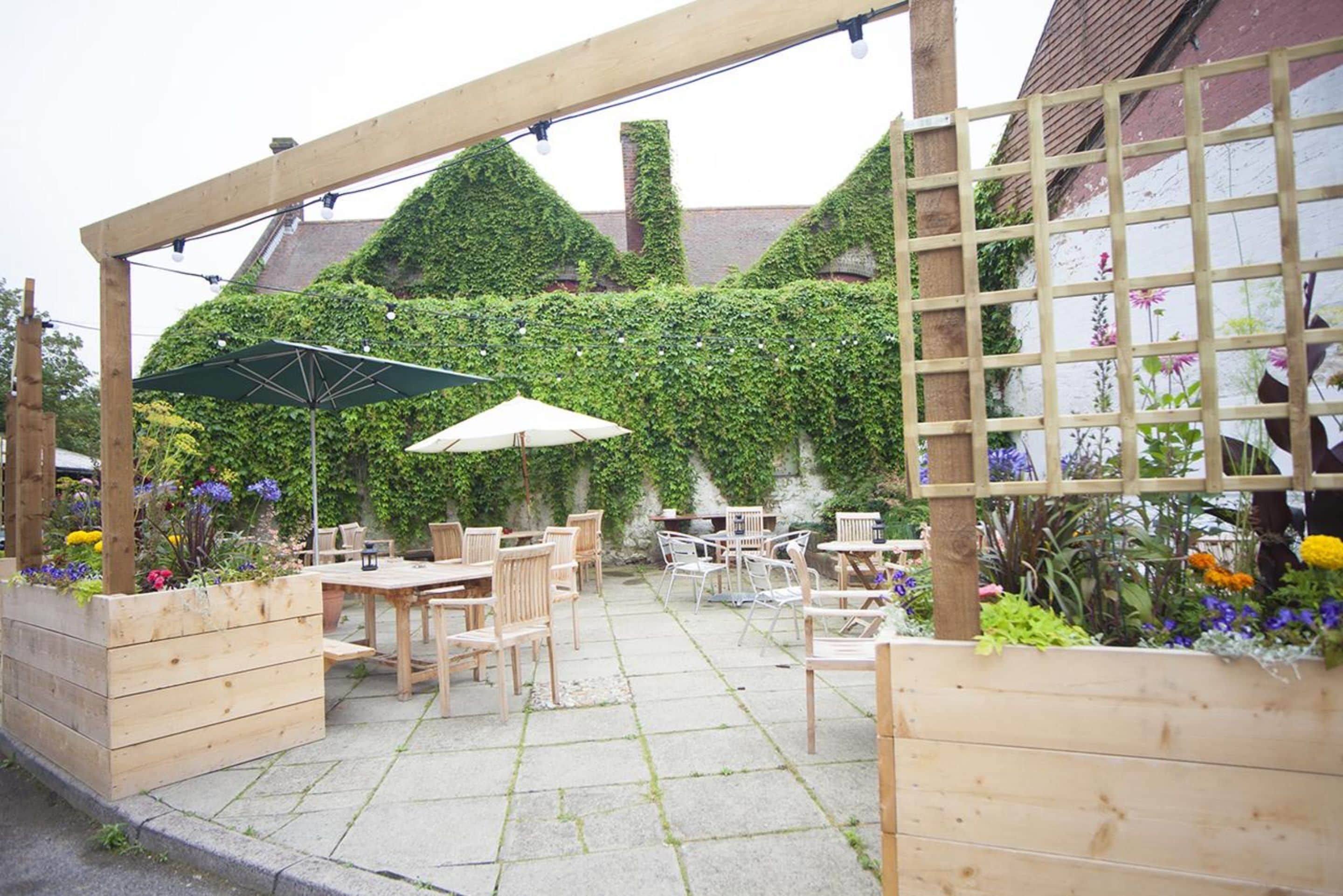 An outdoor patio with wooden furniture and planters, surrounded by a wooden pergola and a lattice fence.