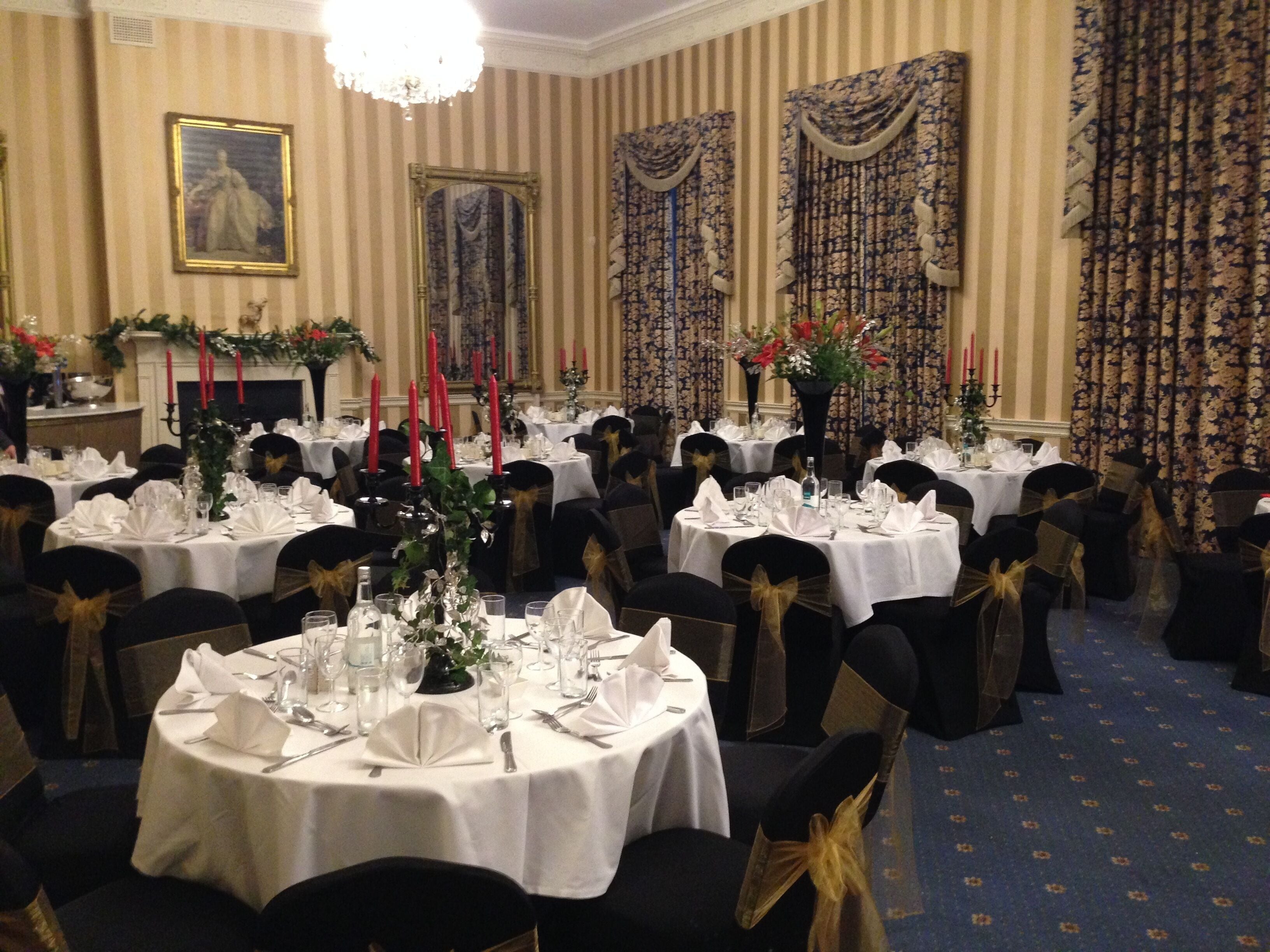 A banquet hall with round tables set for dining, featuring white tablecloths and black chairs with gold sashes.