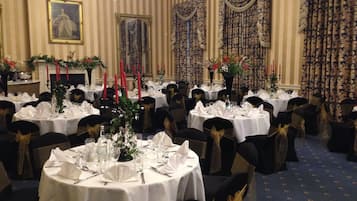 A banquet hall with round tables set for dining, featuring white tablecloths and black chairs with gold sashes.