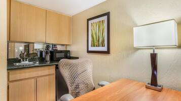 A compact kitchen with wooden cabinets, a sink, a coffee maker, and a chair.