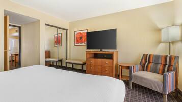 A hotel room with a large bed, a television, a wooden dresser, a striped armchair, and a small table.