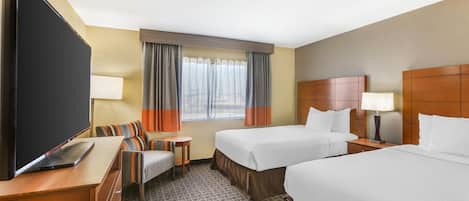 Quarto de hotel com duas camas, uma escrivaninha, uma cadeira, uma televisão e uma janela com cortinas.